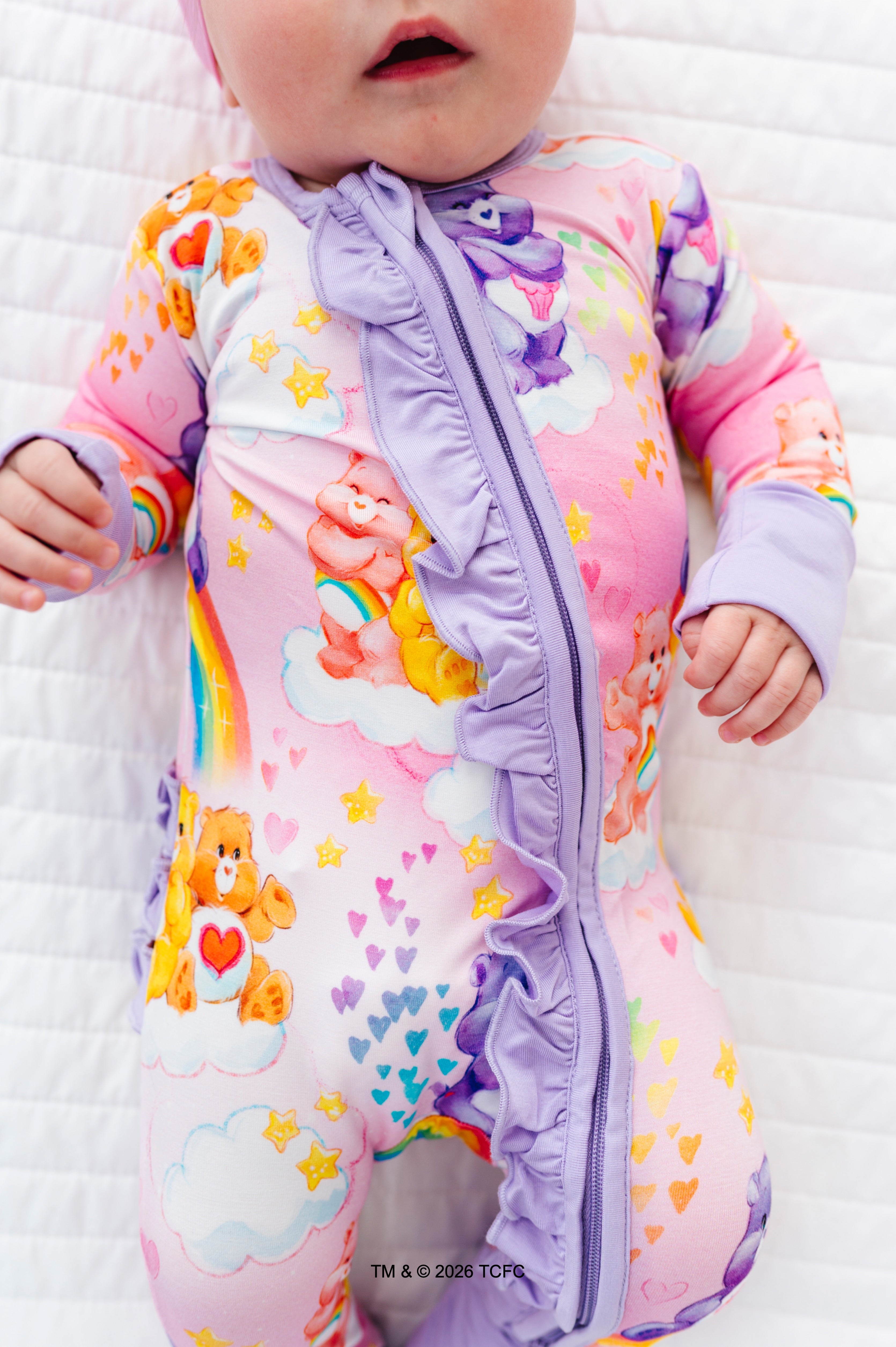 Baby wearing a colorful Care Bears™ sleeper on a white blanket
